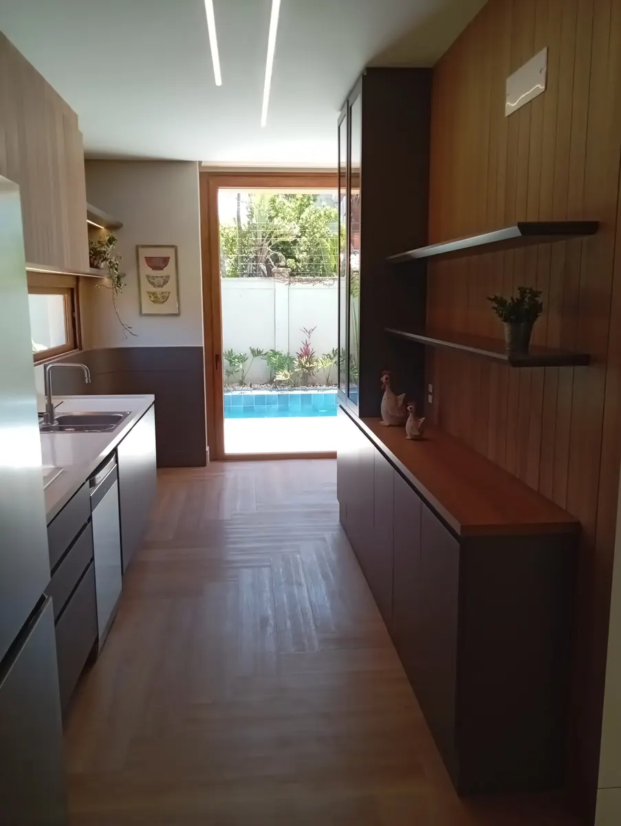 Cozinha em corredor com marcenaria em madeira e painel ripado, com vista para a piscina